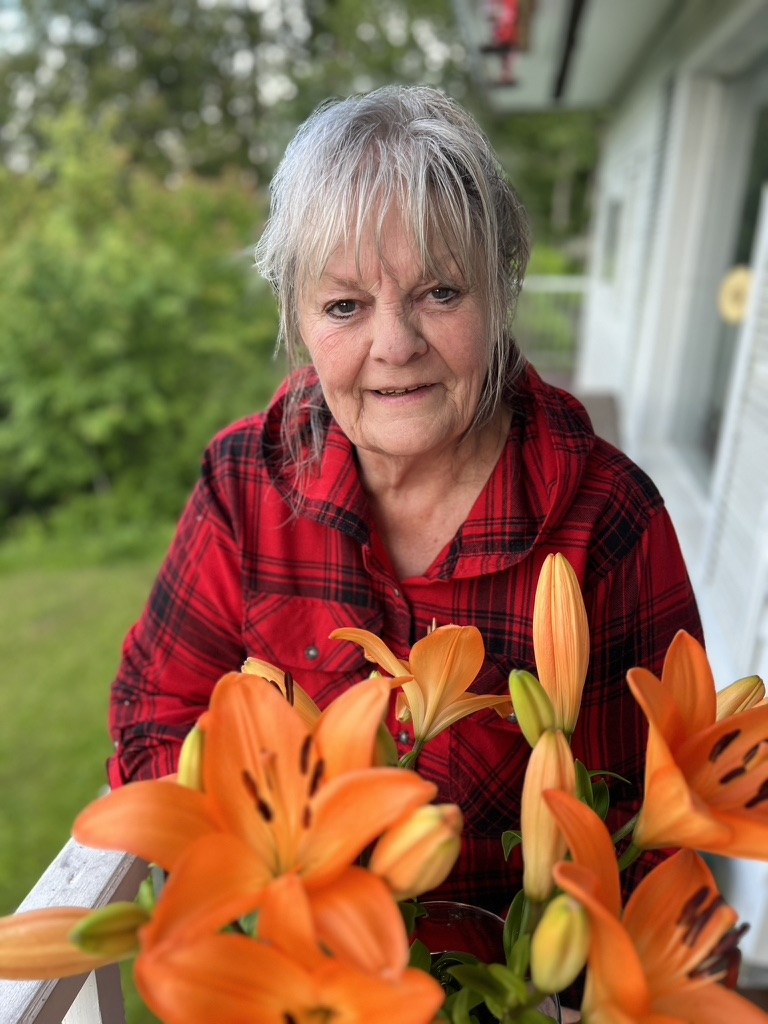 Bette on the porch in a red plaid shirt behind a pot of orange tiger lilies
